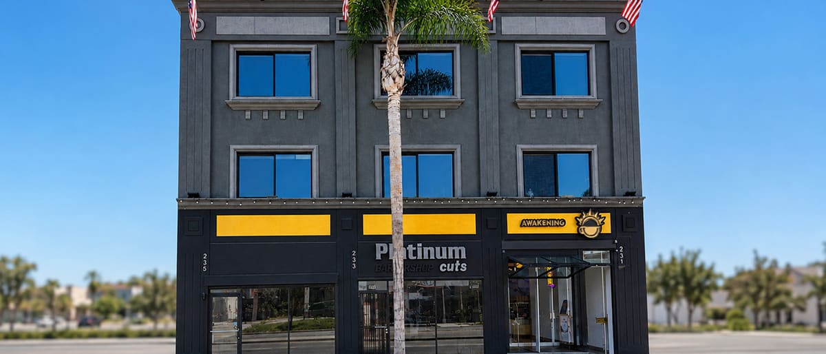 Three-storey charcoal building on La Brea Avenue with yellow sign bands over three ground-floor storefronts and a palm tree in front