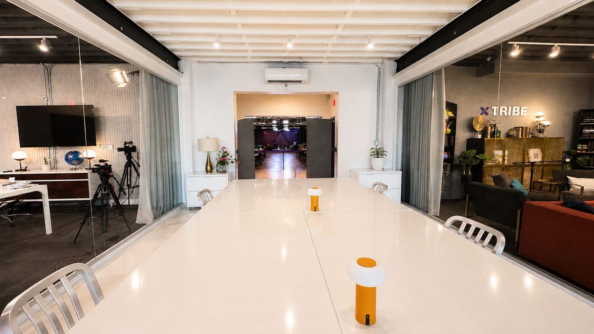 Long white conference table in a bright corridor flanked by glass-walled studios