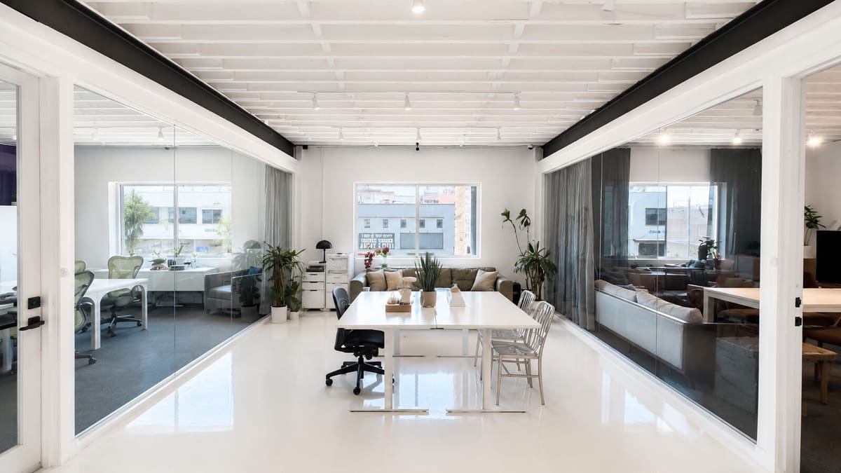 Bright office with a white table, desk chairs and sofa behind glass walls, with street-facing windows
