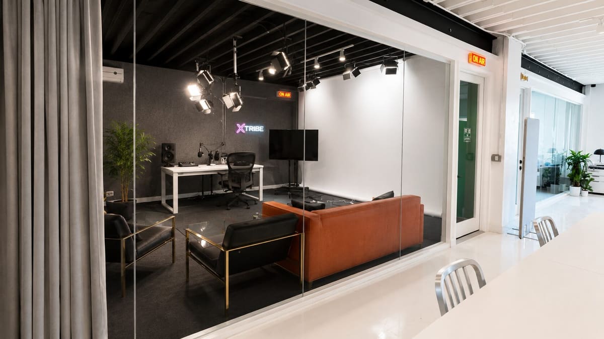 Studio with a rust-colored sofa, desk, track lighting and an xTribe sign seen through glass walls