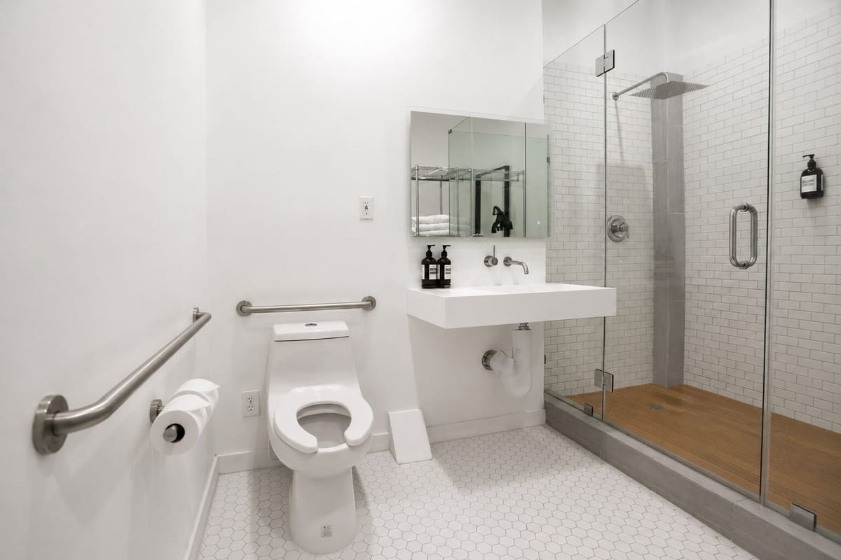 White tiled bathroom with grab bars, a wall-mounted sink and a glass walk-in shower